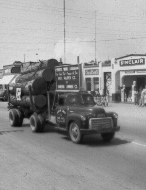 A truck with logs on the back of it driving down the street.